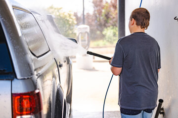 Teen boy washing vehicle in self-service car wash bay