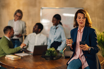 Mature manager using cellphone on meeting of interracial staff at office