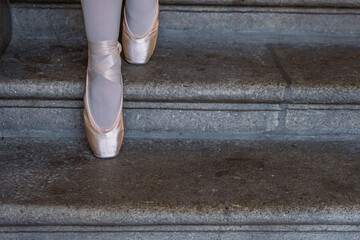 Closeup of ballerina's pointes on the gray stone steps background. Dance sitting on the steps. Ballerina´s feet with pink ballet slippers on. Minimalistic, simple. Copy space. © Dina