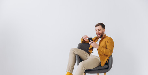 Modern happy millennial man using smartphone and typing on white background