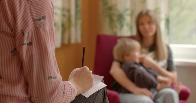 Woman with a child, hand in the foreground writing something on a piece of paper. Case worker or social worker meeting with client to discuss services, assistance, support provided by social services.