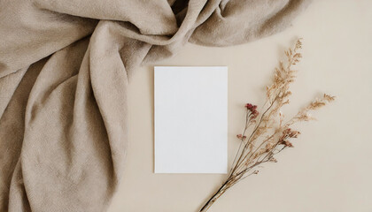 Blank paper sheet card with mockup copy space and dry floral branch and blanket cloth on neutral...