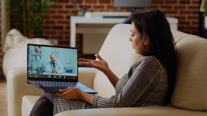Patient sitting on couch, receiving treatment plan from medic during online videocall meeting after...