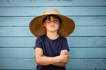 portrait of very serious child in straw hat with folded arms - obrazy, fototapety, plakaty