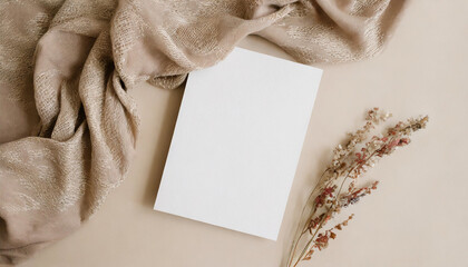 Blank paper sheet card with mockup copy space and dry floral branch and blanket cloth on neutral...