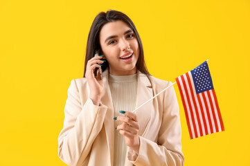Young woman with USA flag talking by mobile phone on yellow background