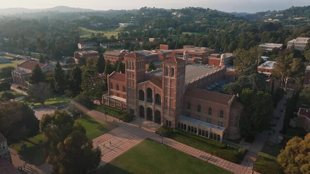 Aerial view of UCLA campus bathed in golden light, showcasing Romanesque Revival and Gothic architecture amid lush greenery, with Royce Hall as the centerpiece.