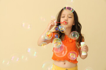 Cute little girl blowing soap bubbles on beige background