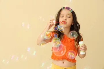 Gardinen Cute little girl blowing soap bubbles on beige background © Pixel-Shot