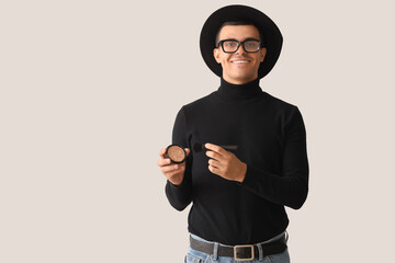 Male makeup artist with brush and highlighter on light background