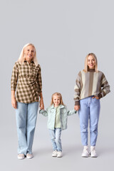 Fototapeta premium Cute little girl with her mother and granny holding hands on light background