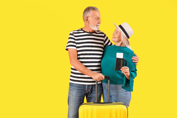 Senior couple with suitcase, passport and ticket on yellow background