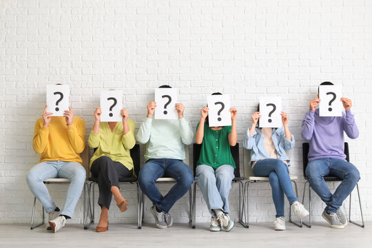 Applicants holding paper sheets with question marks near white brick wall