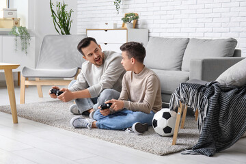 Father and his little son with soccer ball playing video games at home - obrazy, fototapety, plakaty