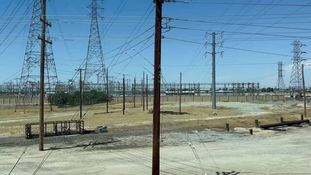 The camera pans over an electrical substation in the San Joaquin Valley region of California. Electrical poles, electrical wires, and other infrastructure dominate the landscape.