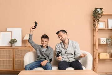 Father and his little son playing video games on sofa at home