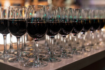 Wine glasses filled with red wine arranged and presented on a table top for self-service by party...