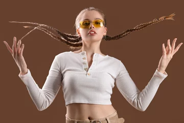 Gardinen Beautiful young woman with stylish sunglasses posing on brown background © Pixel-Shot