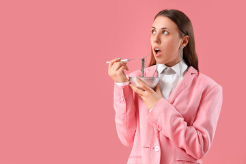 Woman with bowl eating jewelry on pink background