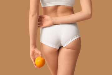 Beautiful young woman with cellulite problem and orange on brown background, back view