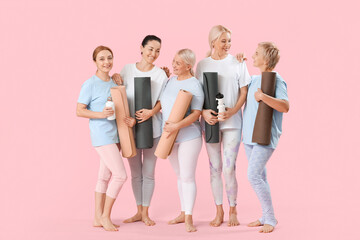 Group of mature women with yoga mats on pink background
