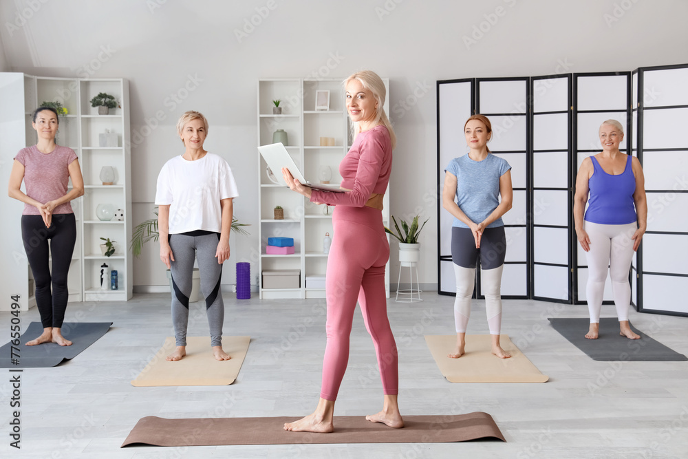 Poster Group of sporty mature women doing yoga with trainer in gym