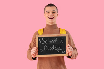 Cheerful male student holding chalkboard with text SCHOOL GOODBYE on pink background. End of school concept