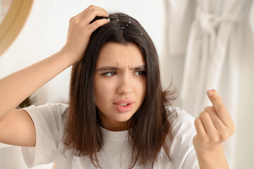 Stressed young woman with dandruff problem in light bathroom