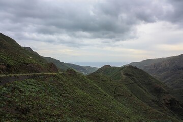 Majestic Mountain Landscape under the Rainy Sky.  The Path Winds through Lush Greenery, with Plenty...