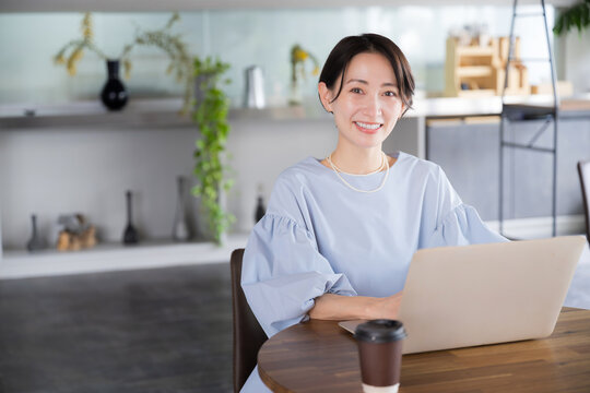 綺麗なオフィスやカフェでパソコンで仕事をする笑顔の美人なアジア系(日本人）女性の全身の広角のビジネスシーン　カメラ目線