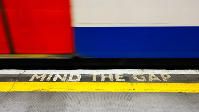 London, UK - March 24, 2024; Mind the Gap sign on edge of London Underground platform with tube passing train