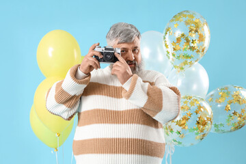Senior man with bunch of balloons and photo camera on blue background