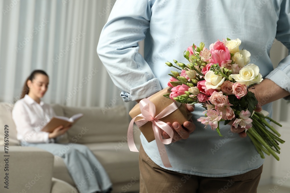 Sticker Man hiding bouquet of flowers and present for his beloved woman indoors, closeup