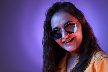 Portrait of beautiful young woman with stylish sunglasses on color background with neon lights