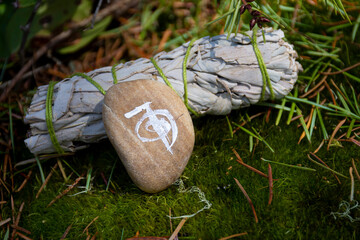 An image of a healing symbol for alternative medicine and a white sage smudge stick on a thick bed of lush green moss. 