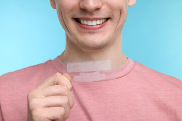 Young man with whitening strips on light blue background, closeup