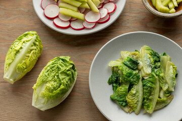A plate with Chinese-style stir-fried lettuce and two heads of fresh mini romaine lettuce. A salad...