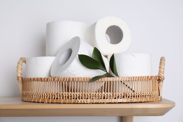 Toilet paper rolls and green leaves on wooden table near white wall