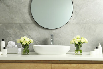 Beautiful roses, bath accessories, sink and mirror in bathroom