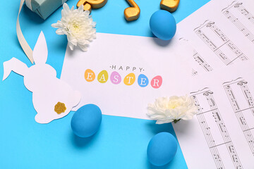 Composition with greeting card, music notes and Easter decor on blue background