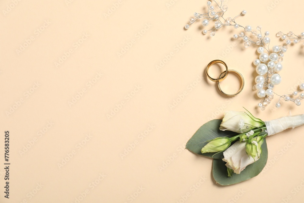 Wall mural Wedding stuff. Stylish boutonniere, rings and decor on beige background, flat lay. Space for text