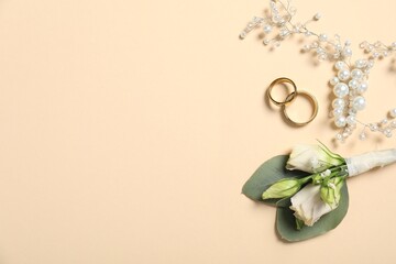 Wedding stuff. Stylish boutonniere, rings and decor on beige background, flat lay. Space for text