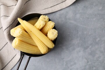 Tasty fresh yellow baby corns in dish on grey table, top view. Space for text