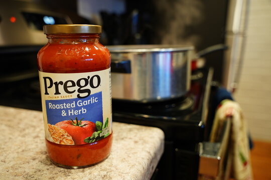 A glass jar of Prego Roasted Garlic and Herb spaghetti sauce sits on a counter waiting to be used. 