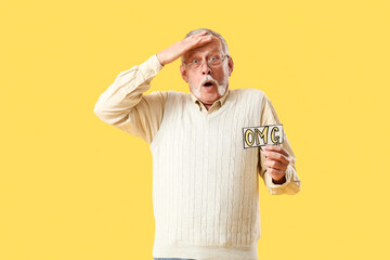 Shocked senior man holding speech bubble with word OMG on yellow background