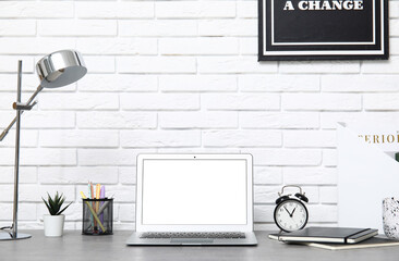 Stylish workplace with modern laptop, lamp and stationery near white brick wall