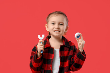 Happy little girl in checkered pajamas with toothbrush and dental floss on red background