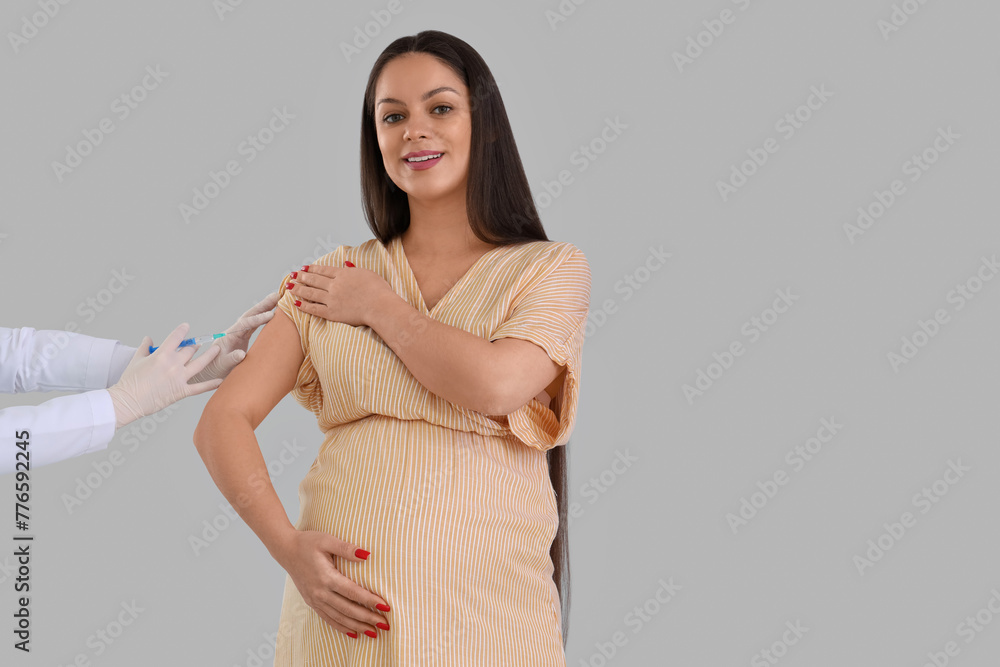 Wall mural Young pregnant woman receiving vaccine on light background