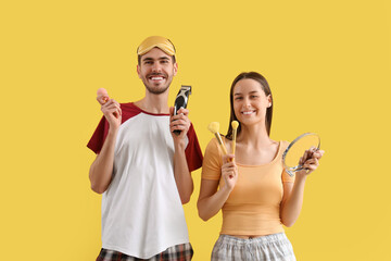 Young loving couple with trimmer and makeup accessories on yellow background