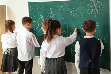 Cute little pupils drawing on blackboard in classroom, back view. School holidays concept